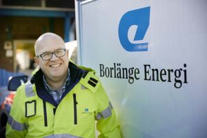 Glad varselklädd medarbetare på Borlänge Energi framför skylt.